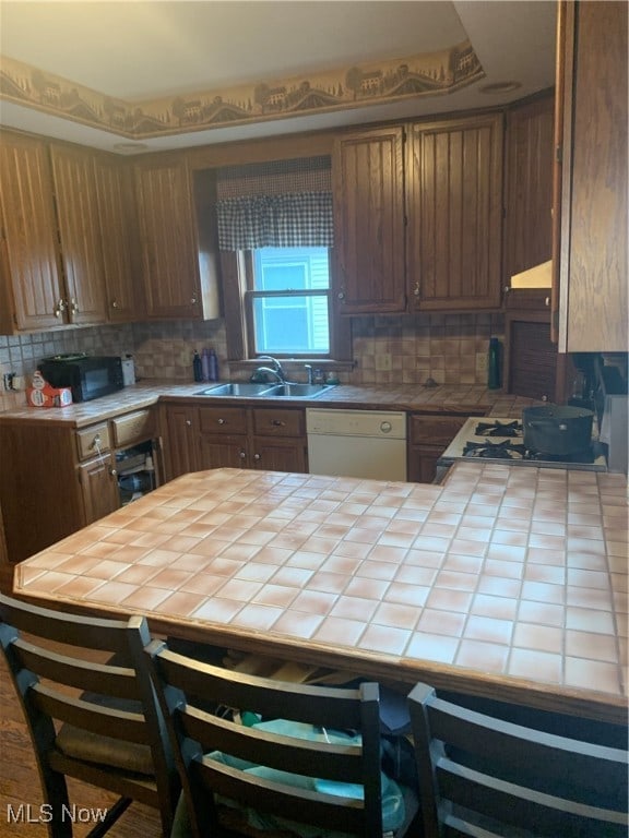 kitchen with tile countertops, decorative backsplash, sink, and white dishwasher