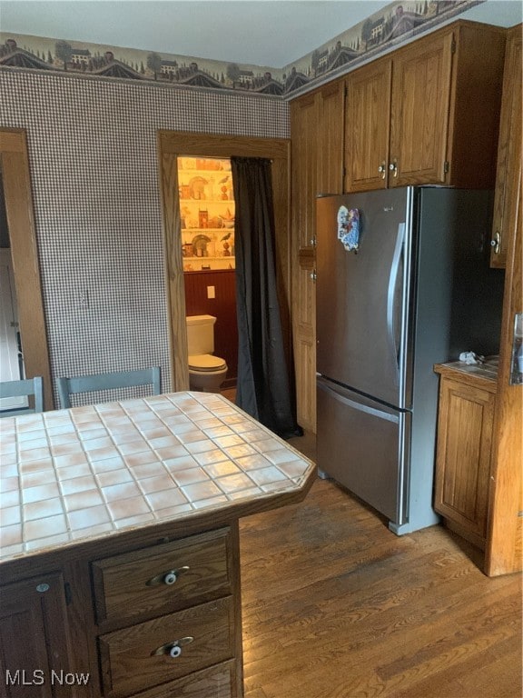 kitchen featuring hardwood / wood-style floors, tile counters, and stainless steel refrigerator