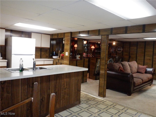 kitchen with a paneled ceiling, light colored carpet, sink, white fridge, and wood walls