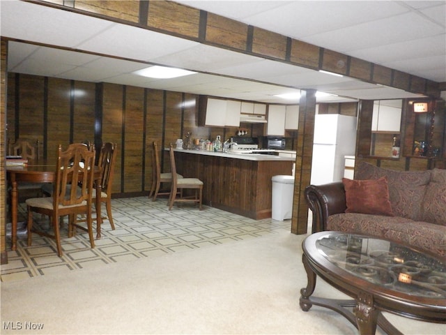 living room featuring light colored carpet, a drop ceiling, and wood walls