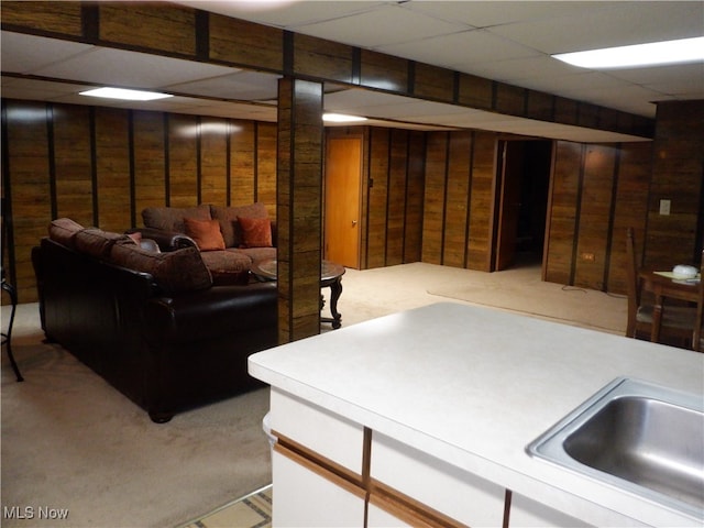 basement featuring a paneled ceiling, wood walls, and sink