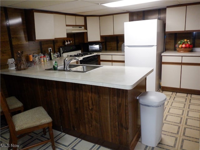 kitchen featuring a drop ceiling, white appliances, sink, kitchen peninsula, and a breakfast bar area