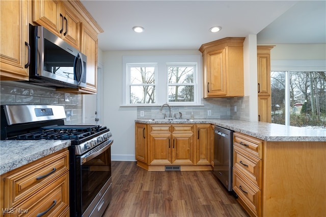 kitchen featuring decorative backsplash, kitchen peninsula, stainless steel appliances, sink, and dark hardwood / wood-style floors