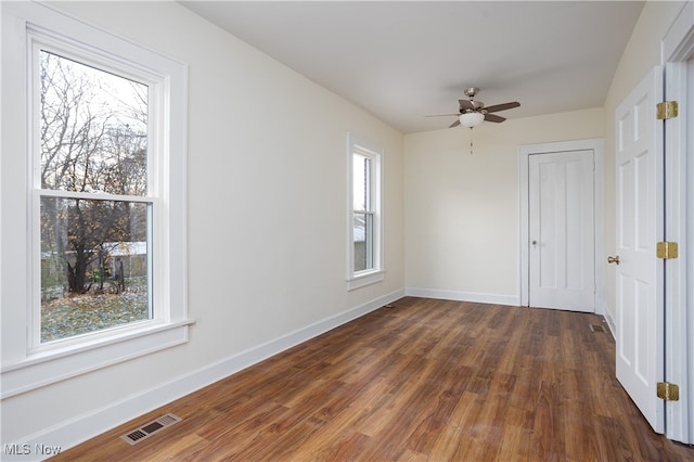 empty room with ceiling fan, plenty of natural light, and dark wood-type flooring