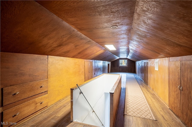 additional living space with wooden walls, lofted ceiling, and light wood-type flooring