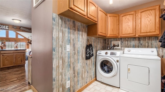 clothes washing area featuring cabinets, a textured ceiling, washing machine and dryer, and wood walls