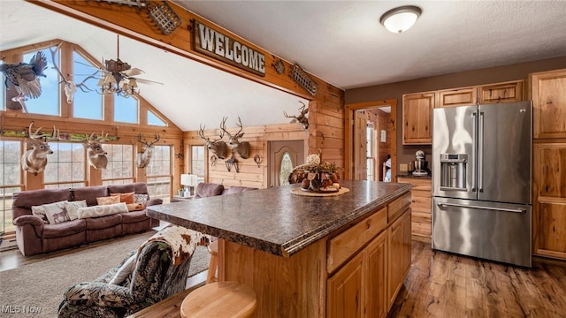 kitchen featuring stainless steel fridge, ceiling fan, light hardwood / wood-style flooring, a kitchen island, and wood walls