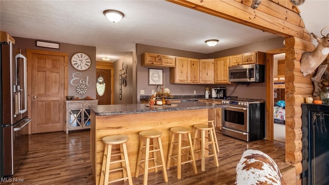 kitchen with appliances with stainless steel finishes, a kitchen breakfast bar, light brown cabinets, a center island, and dark hardwood / wood-style floors