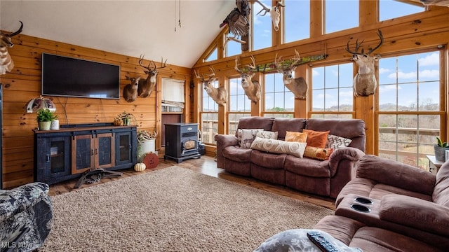 living room featuring a wood stove, wood walls, hardwood / wood-style floors, and high vaulted ceiling