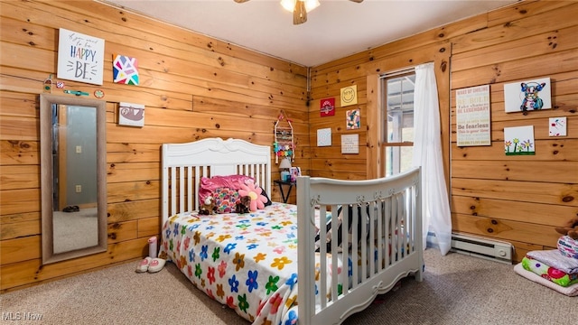 carpeted bedroom featuring baseboard heating, wood walls, and ceiling fan