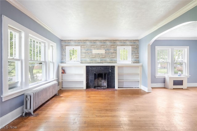 unfurnished living room featuring light hardwood / wood-style floors, radiator heating unit, a fireplace, and ornamental molding