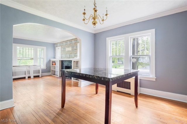 dining room featuring hardwood / wood-style floors, a tiled fireplace, crown molding, and an inviting chandelier