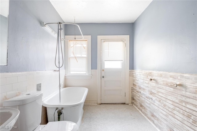 bathroom featuring a bathing tub, tile patterned flooring, toilet, and tile walls