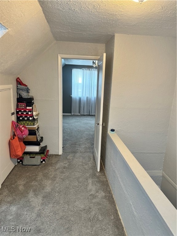 hall featuring carpet flooring, a textured ceiling, and lofted ceiling