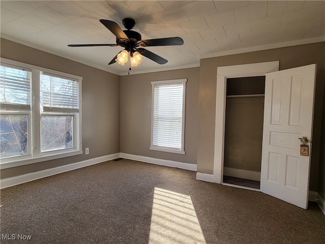 unfurnished bedroom featuring multiple windows, dark colored carpet, ceiling fan, and ornamental molding