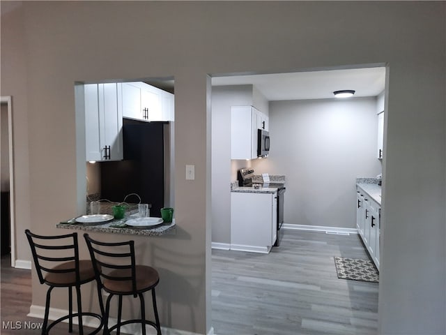 kitchen with electric stove, white cabinetry, black refrigerator, and light stone countertops