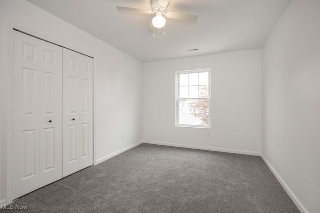 unfurnished bedroom with dark colored carpet, ceiling fan, and a closet