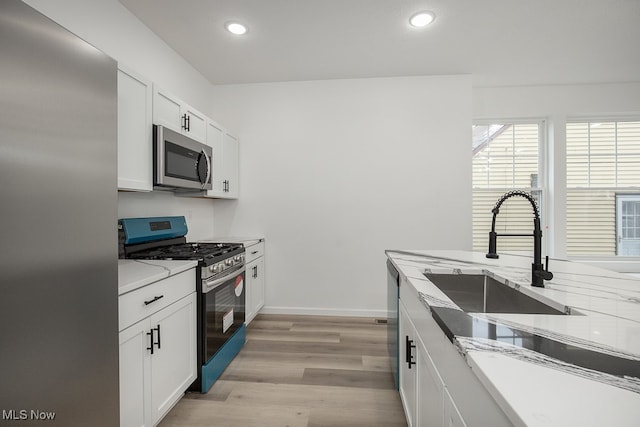 kitchen with light stone countertops, appliances with stainless steel finishes, light wood-type flooring, sink, and white cabinetry