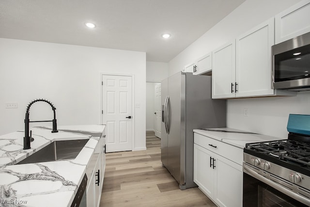 kitchen featuring white cabinetry, sink, stainless steel appliances, light stone counters, and light wood-type flooring