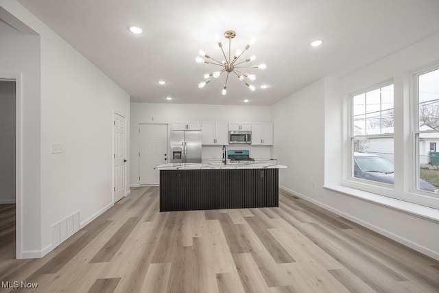 kitchen with white cabinetry, stainless steel appliances, a chandelier, light hardwood / wood-style floors, and a kitchen island with sink