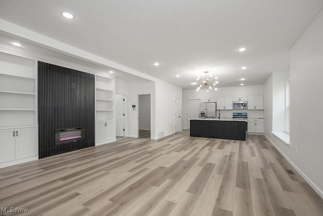 unfurnished living room featuring a chandelier, a textured ceiling, and light hardwood / wood-style floors