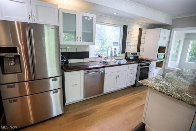 kitchen featuring stainless steel appliances, dark stone counters, decorative backsplash, white cabinets, and light wood-type flooring