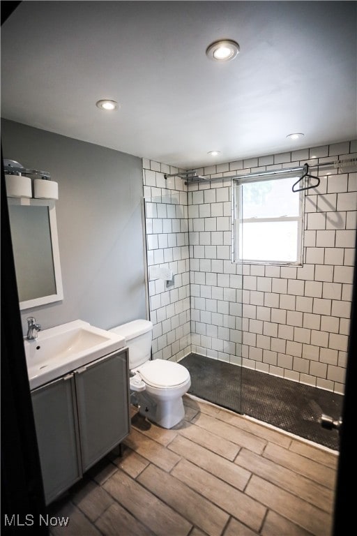 bathroom featuring hardwood / wood-style flooring, vanity, toilet, and a tile shower