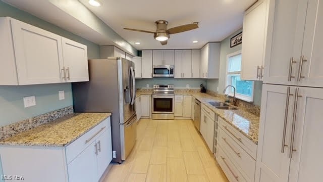 kitchen with sink, ceiling fan, light stone countertops, appliances with stainless steel finishes, and white cabinetry