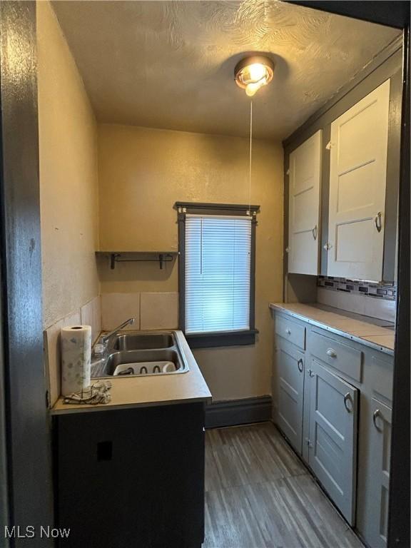 kitchen with a textured ceiling, wood-type flooring, sink, backsplash, and gray cabinets