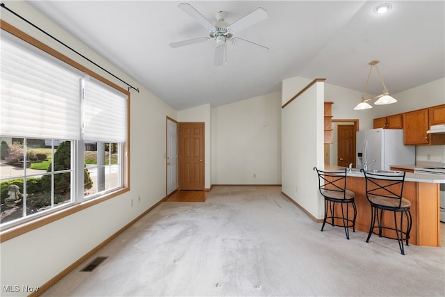 kitchen featuring a breakfast bar, stainless steel range, white fridge with ice dispenser, and light colored carpet