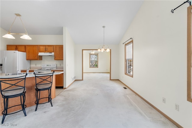 kitchen featuring a notable chandelier, light colored carpet, decorative light fixtures, white appliances, and a kitchen bar