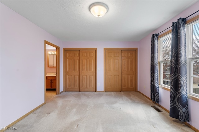 unfurnished bedroom featuring two closets, connected bathroom, light colored carpet, and a textured ceiling