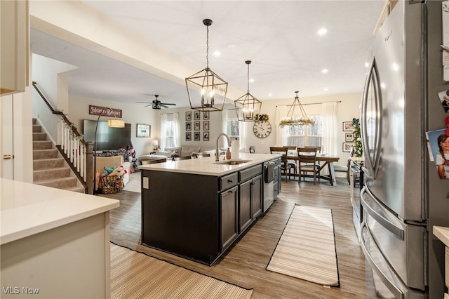 kitchen with sink, stainless steel appliances, light hardwood / wood-style floors, decorative light fixtures, and a center island with sink