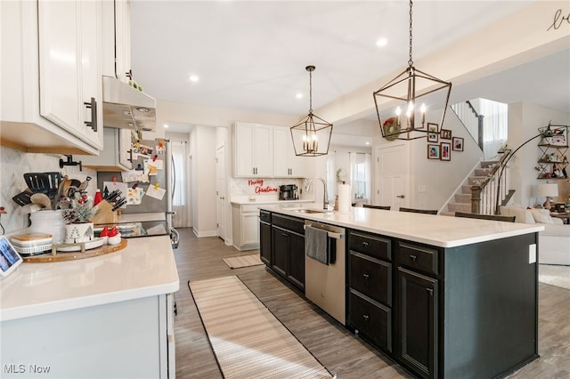 kitchen with stainless steel dishwasher, sink, a center island with sink, white cabinets, and hanging light fixtures