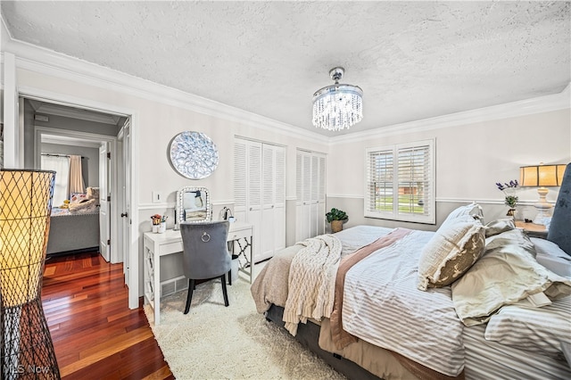 bedroom with wood-type flooring, a textured ceiling, multiple closets, and ornamental molding