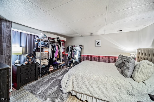 bedroom with a paneled ceiling, wood walls, and hardwood / wood-style floors