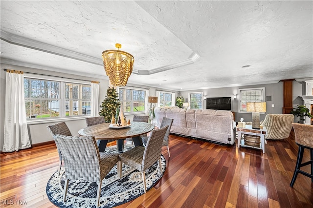 dining space with dark wood-type flooring, a raised ceiling, a notable chandelier, crown molding, and a textured ceiling