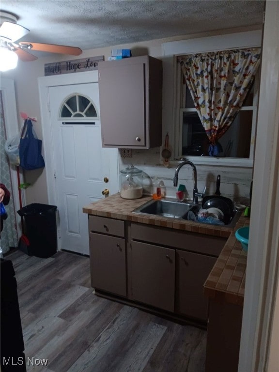 kitchen with hardwood / wood-style flooring, tile counters, a textured ceiling, and sink