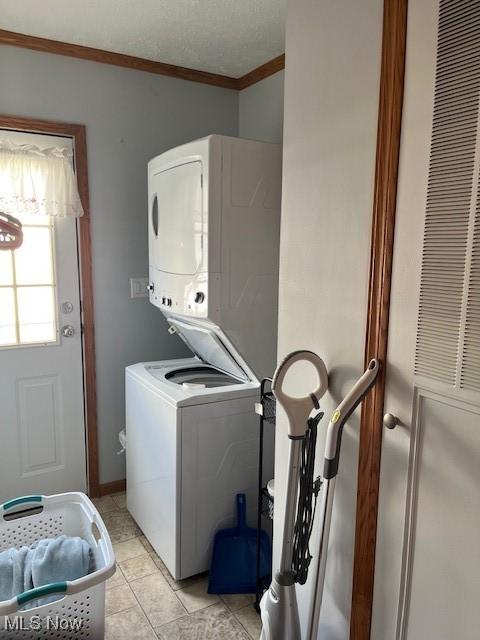 laundry room featuring light tile patterned floors, stacked washing maching and dryer, and ornamental molding