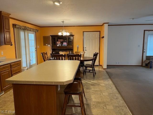 kitchen featuring a center island, an inviting chandelier, crown molding, pendant lighting, and a kitchen bar