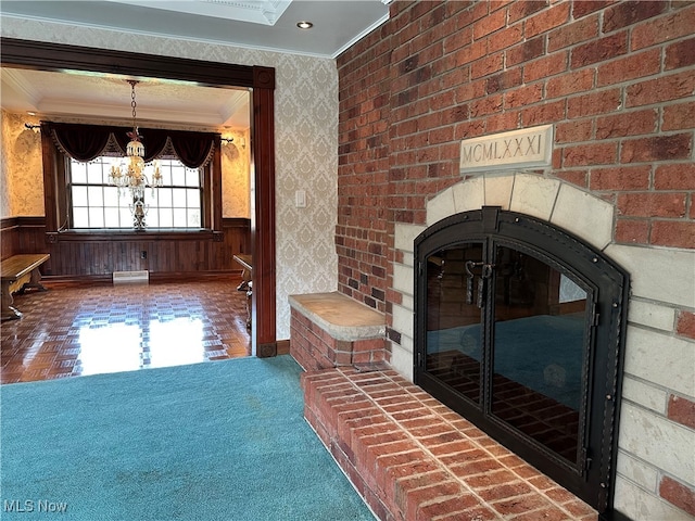 unfurnished living room with a brick fireplace, ornamental molding, wooden walls, and a chandelier