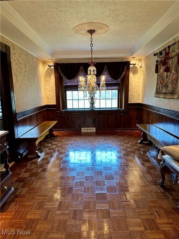 unfurnished dining area featuring a textured ceiling, dark parquet flooring, crown molding, and an inviting chandelier