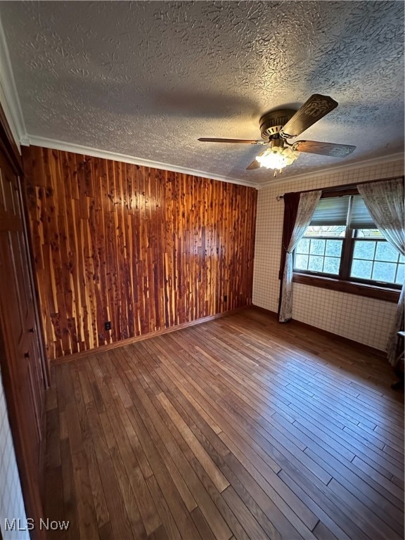 empty room featuring ornamental molding, a textured ceiling, ceiling fan, hardwood / wood-style flooring, and wood walls