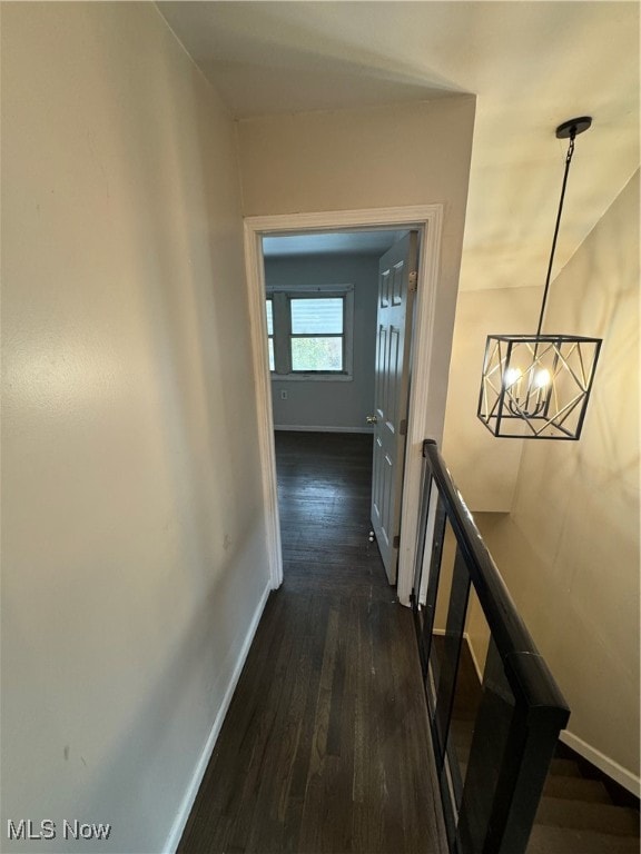 hallway with dark wood-type flooring and a notable chandelier