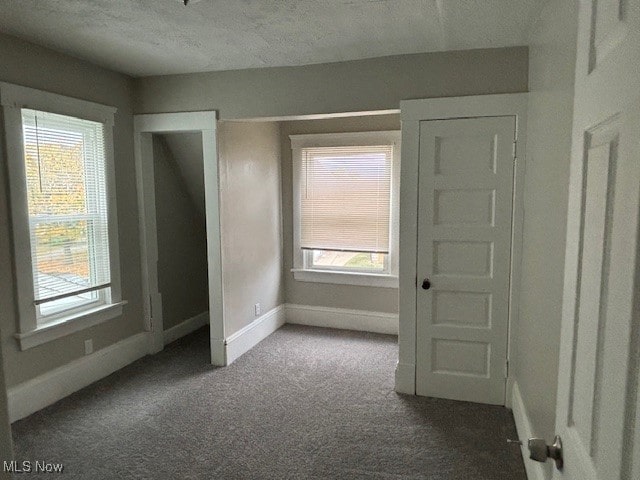 empty room with dark colored carpet, a textured ceiling, and a wealth of natural light