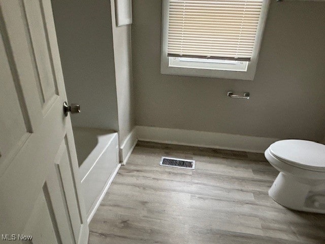 bathroom featuring toilet, wood-type flooring, and a tub