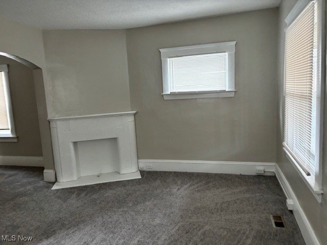 unfurnished living room featuring a textured ceiling and dark colored carpet