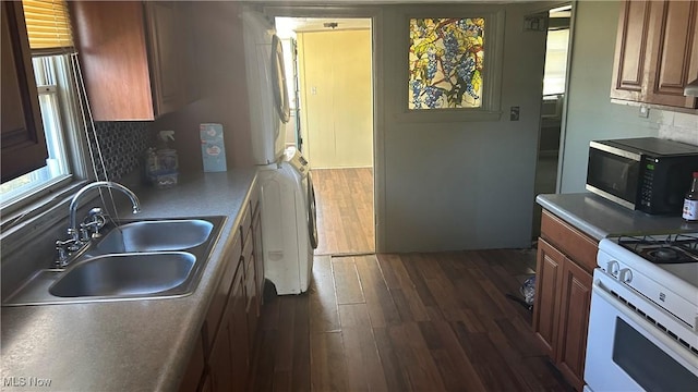 kitchen with backsplash, sink, white range with gas cooktop, stacked washer and dryer, and dark hardwood / wood-style flooring