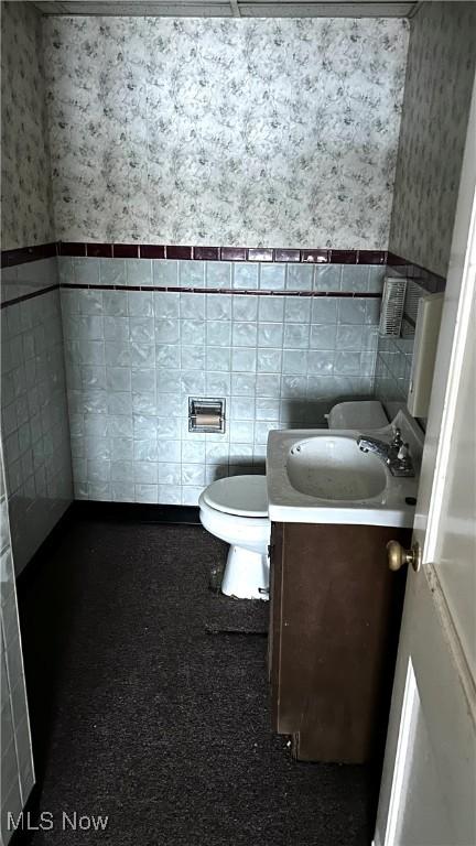 bathroom featuring toilet, tile walls, and vanity