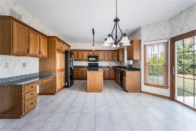 kitchen featuring dark stone counters, black appliances, pendant lighting, a notable chandelier, and a kitchen island